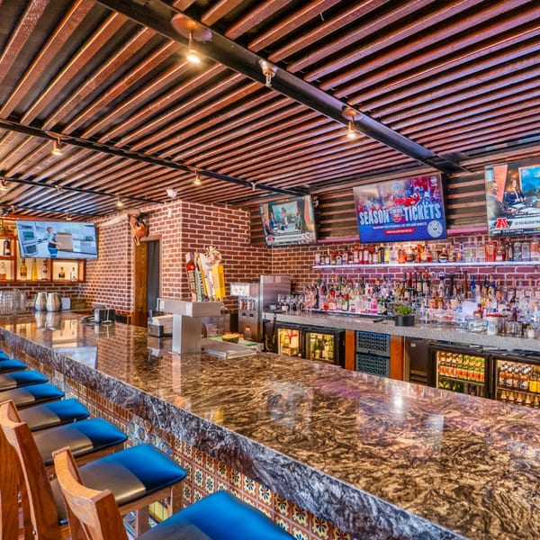 Guapo's Cocina & Bar's long, well-stocked bar with blue stools, brick walls, and multiple TVs.