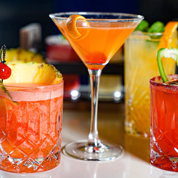 Three vibrant Guapo's Cocina & Bar cocktails, garnished with fruit, on a white bar.