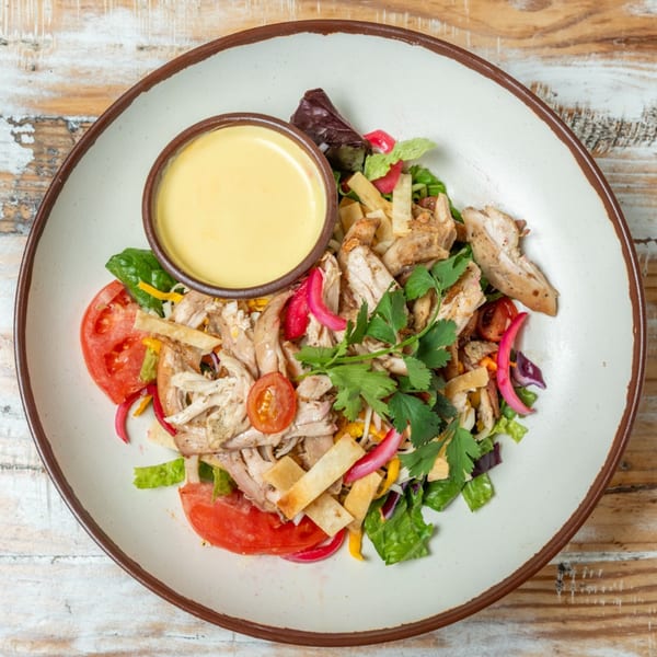 Guapo's chicken salad with tomatoes, red onion, tortilla strips, cilantro, and a side of dressing.