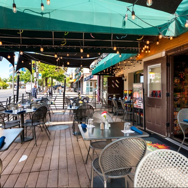 Guapo's Cocina & Bar's inviting outdoor patio with tables, chairs, and string lights under green awnings.