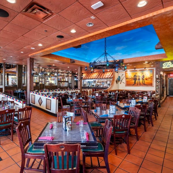 Spacious Guapo's Cocina & Bar dining room with tables, chairs, a bar, and a blue sky ceiling mural.