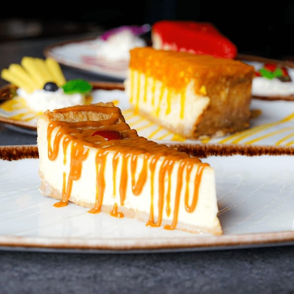 A slice of cheesecake with caramel drizzle, with other cheesecakes in the background.