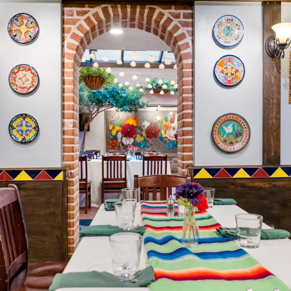 A Guapo's dining room with a colorful serape runner on a table and decorative plates on the walls.