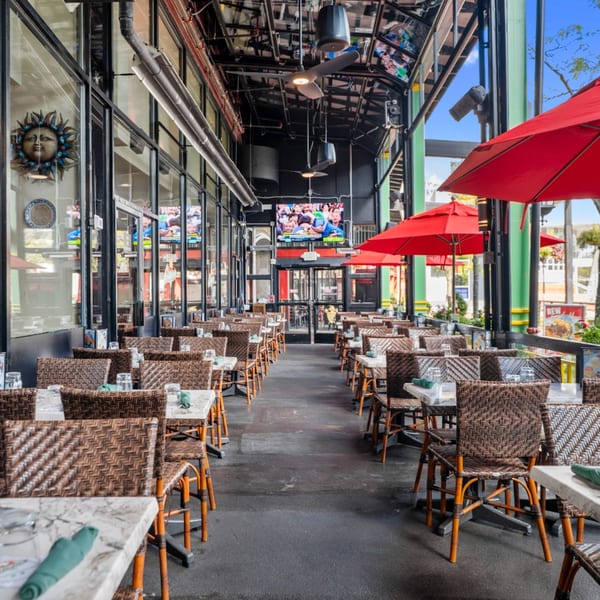 Guapo's Cocina & Bar's outdoor patio with rows of tables, wicker chairs, and red umbrellas.