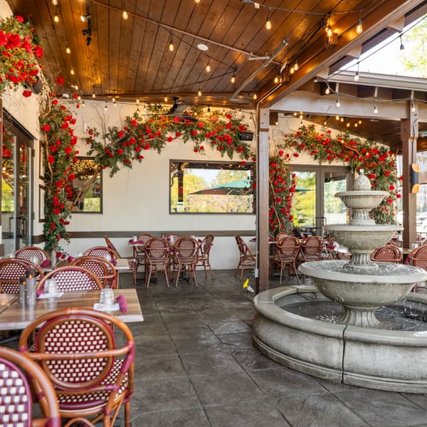 Guapo's Cocina & Bar's outdoor patio with red floral decor, string lights, and a stone fountain.