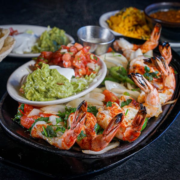 Sizzling shrimp fajitas with onions, peppers, guacamole, pico de gallo, and rice at Guapo's Cocina & Bar.