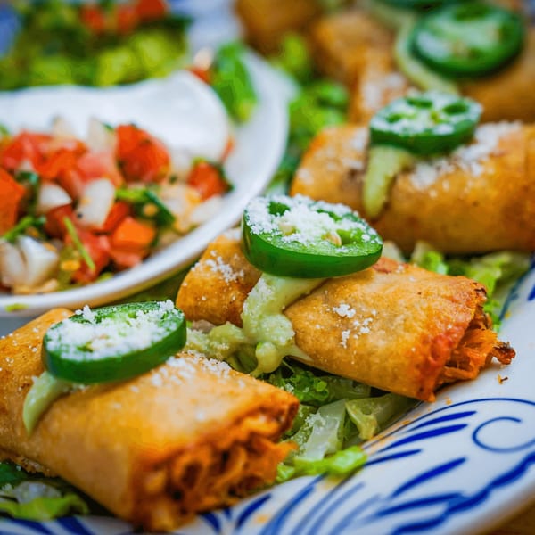 Crispy Mexican flautas topped with jalapeños, cheese, and green sauce, served with pico de gallo.