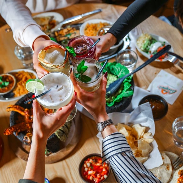 Four people toast colorful cocktails over a table laden with Mexican food at Guapo's Cocina & Bar.