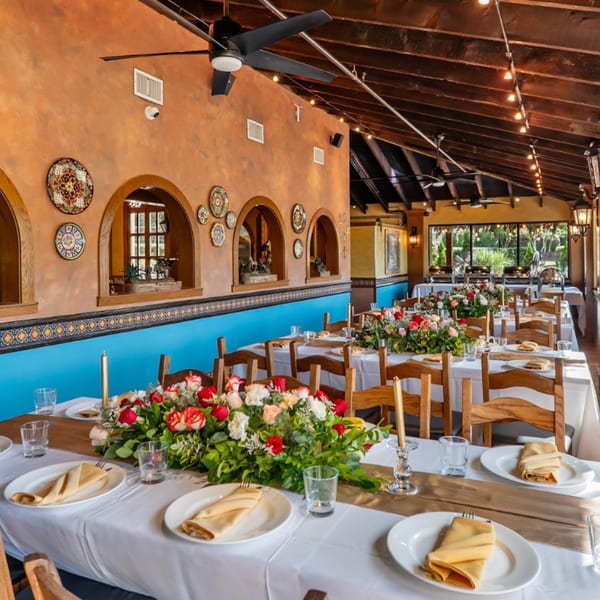 Long tables set with white tablecloths, floral centerpieces, and place settings in a Mexican restaurant.