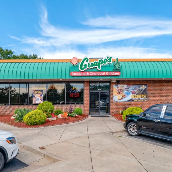 Exterior of Guapo's Taqueria & Charcoal Chicken, a brick building with a green awning and signage.