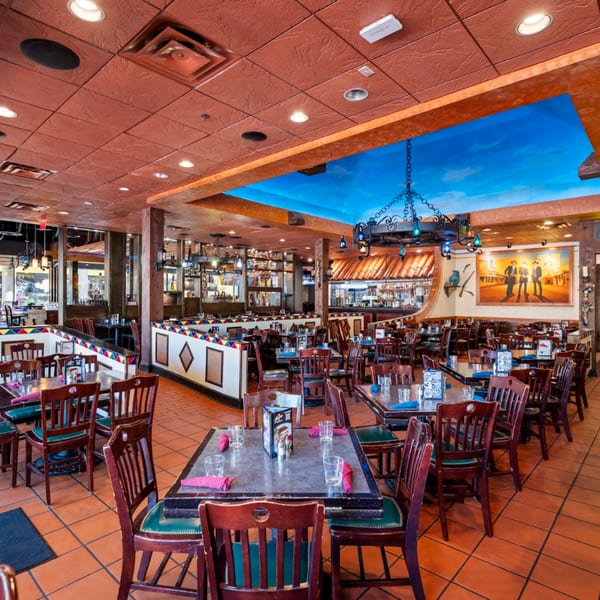 Spacious Guapo's Cocina & Bar dining room with terracotta tiles, wooden tables, and a blue sky ceiling mural.