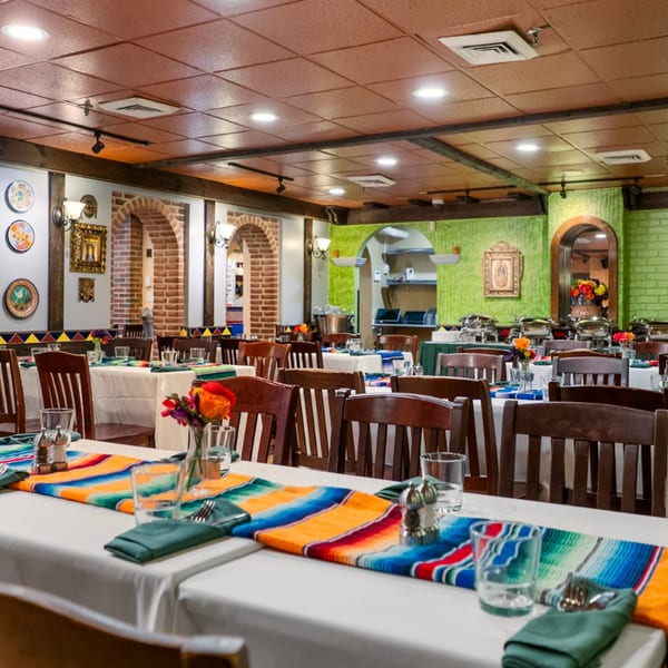 Guapo's Cocina & Bar dining room with tables set with colorful serape runners and dark wooden chairs.