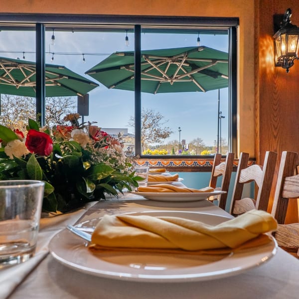 Set table with floral centerpiece, white plates, yellow napkins, and outdoor patio view.