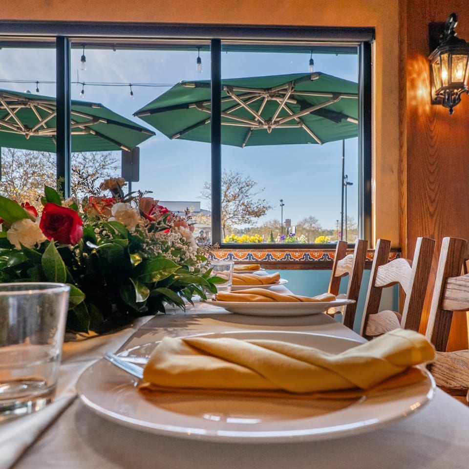 Set table with floral centerpiece, white plates, yellow napkins, and outdoor patio view.