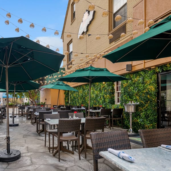 Guapo's Cocina & Bar's outdoor patio with green umbrellas, wicker chairs, and a living wall.