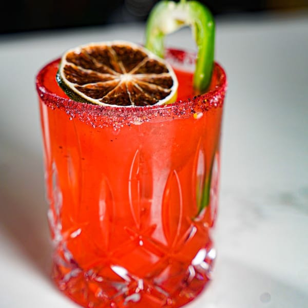 Guapo's Cocina & Bar's red cocktail with a dried lime slice and green pepper garnish.