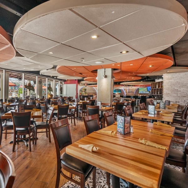 Spacious dining room at Guapo's Cocina & Bar with wooden tables, dark chairs, and large windows.
