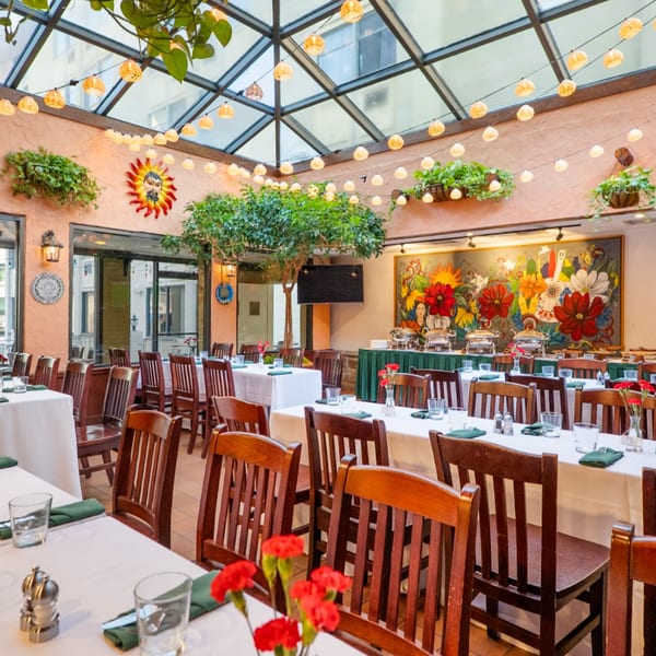 Guapo's Cocina & Bar dining room with set tables, a buffet, and a colorful mural under a skylight.