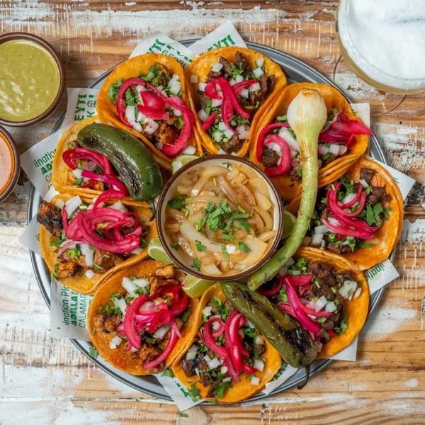A platter of Guapo's Mexican tacos with various fillings, pickled onions, grilled peppers, and sauces.