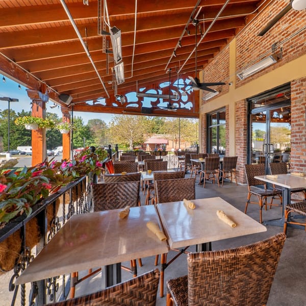 Guapo's Cocina & Bar's outdoor patio with empty tables, wicker chairs, and brick walls.