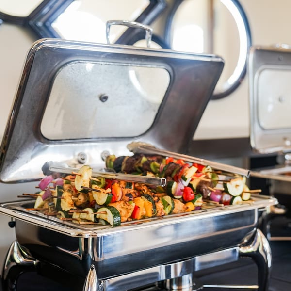 Grilled chicken and vegetable skewers, including zucchini, bell peppers, and onions, in a chafing dish.