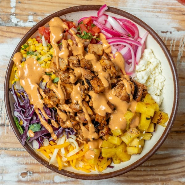 Overhead view of a colorful Guapo's Cocina & Bar Mexican bowl with chicken, corn, pineapple, and sauces.