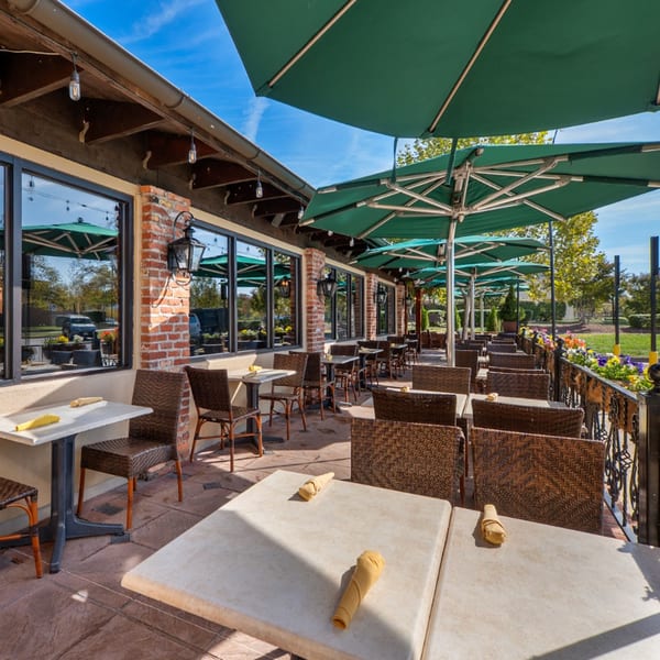 Guapo's Cocina & Bar's outdoor patio with tables, chairs, and green umbrellas under a blue sky.