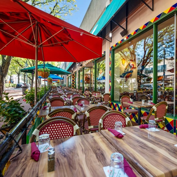Outdoor patio of Guapo's Cocina & Bar with red umbrellas, wooden tables, and red and white chairs.