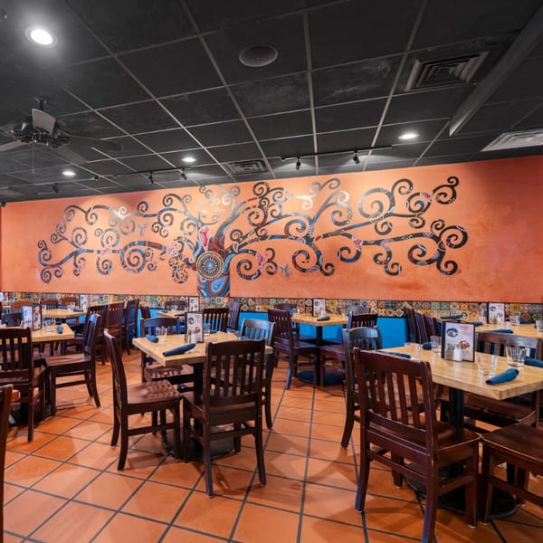 Guapo's Cocina & Bar dining room with an orange wall mural of a tree and set tables.
