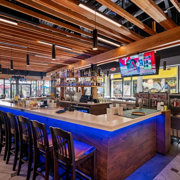 Guapo's Cocina & Bar's spacious bar area with blue under-lighting, bar stools, and a TV.