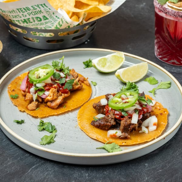 Two Guapo's tacos, one chicken and one steak, with lime wedges on a gray plate.