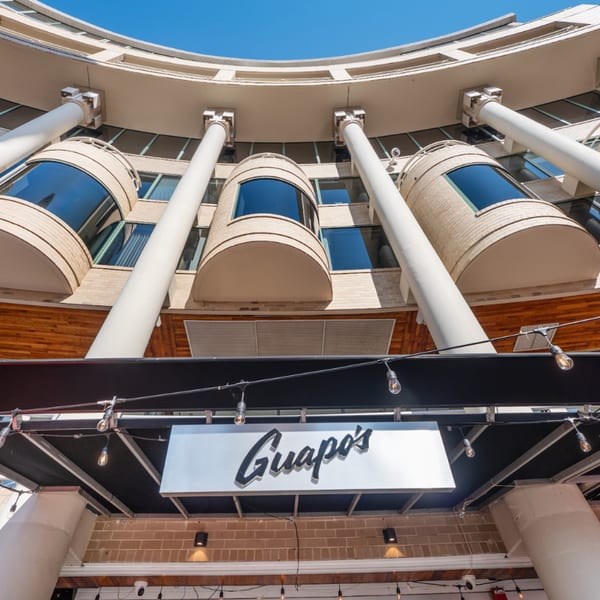 Guapo's restaurant sign with string lights, below a curved building with large columns and windows.