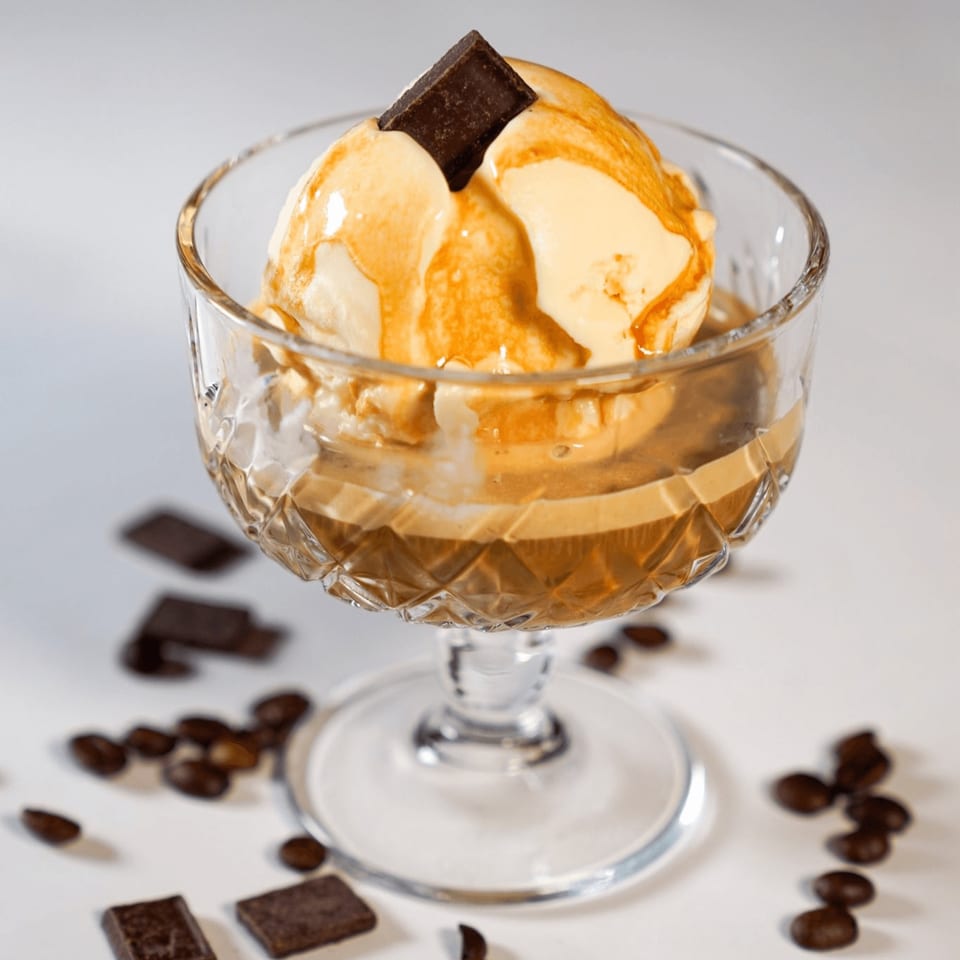 Affogato dessert with vanilla ice cream, espresso, chocolate square, and coffee beans in a glass.