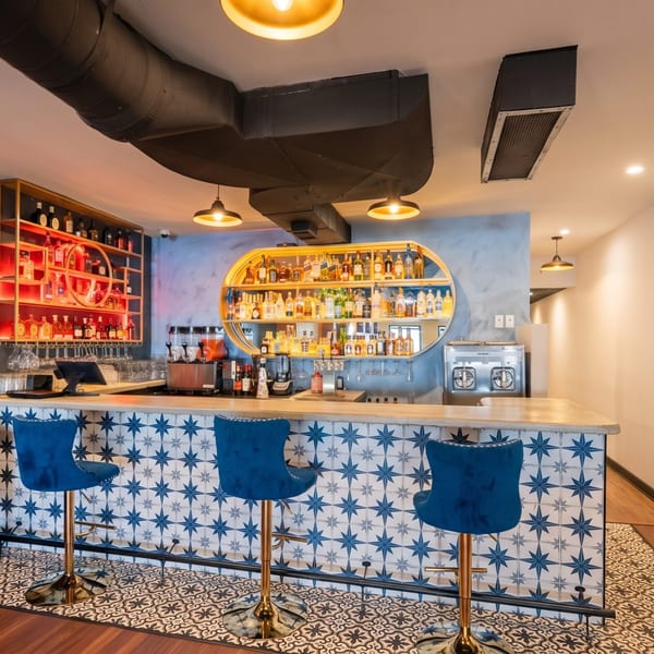 A vibrant bar with blue and white star-patterned tiles, blue velvet bar stools, and liquor bottles on shelves.