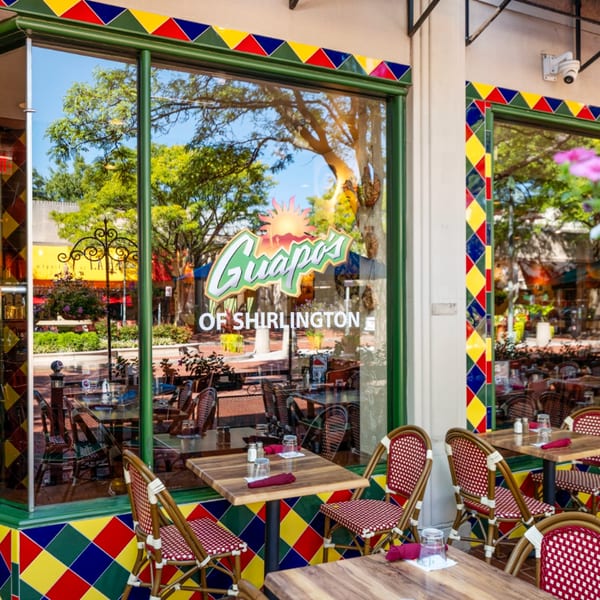 Guapo's Cocina & Bar exterior with colorful tiles, outdoor seating, and a large window reflecting trees.