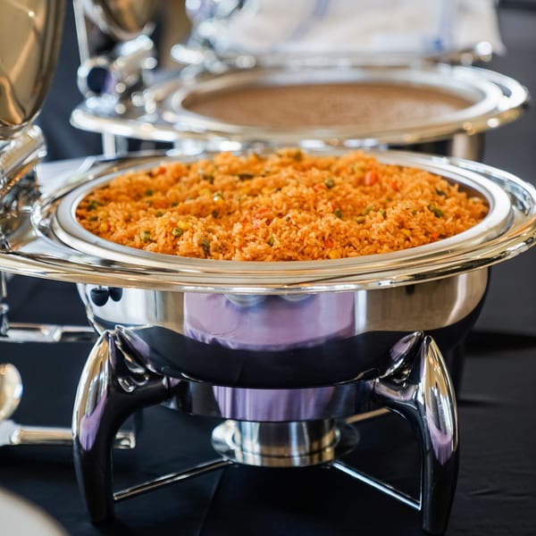 Mexican rice with vegetables in a silver chafing dish on a black tablecloth.
