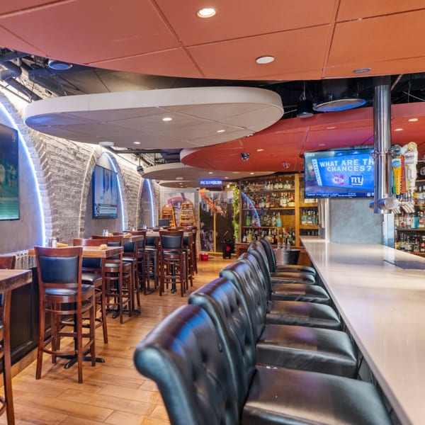 Interior of Guapo's Cocina & Bar, showing a long bar with stools, dining tables, and brick archways.