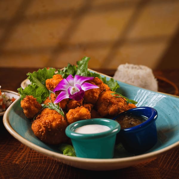 Guapo's Cocina & Bar's fried chicken bites with lettuce, a purple orchid, and two dipping sauces.