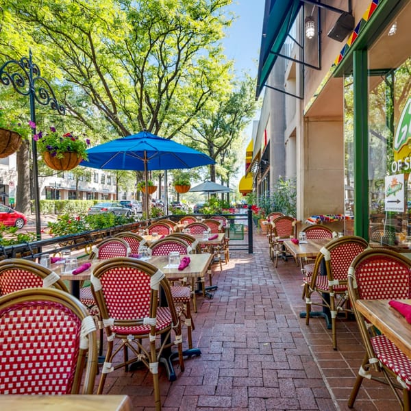 Guapo's Cocina & Bar's outdoor patio with red and white chairs, wooden tables, and blue umbrellas.