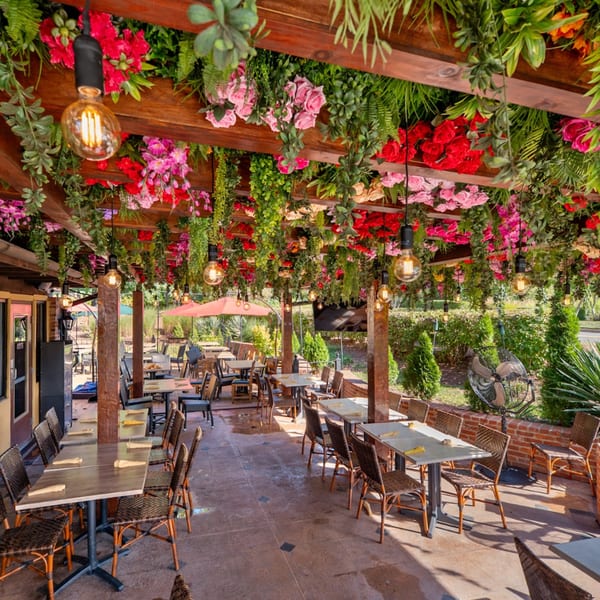 Guapo's Cocina & Bar's outdoor patio with tables, chairs, and a ceiling adorned with colorful flowers and greenery.