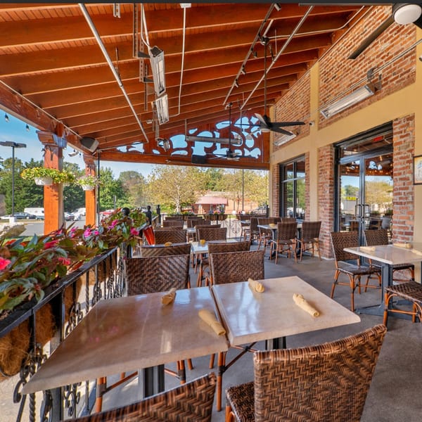 Guapo's Cocina & Bar's outdoor patio with wicker chairs, light-colored tables, and brick walls.