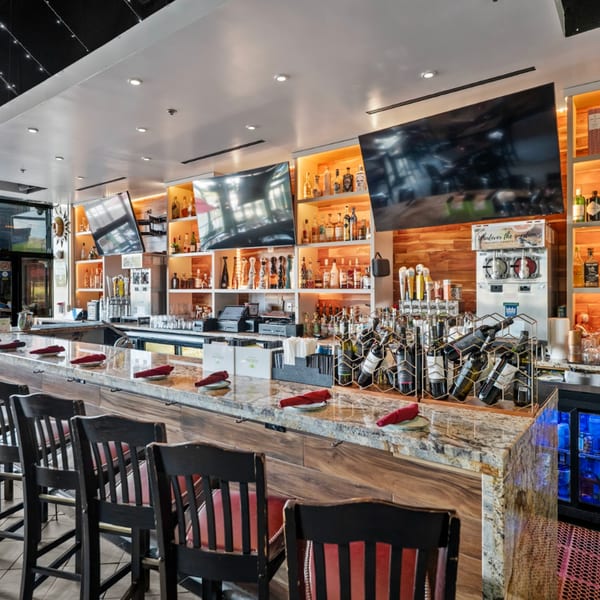 A long, well-lit bar at Guapo's Cocina & Bar with stools, liquor bottles, TVs, and wine racks.