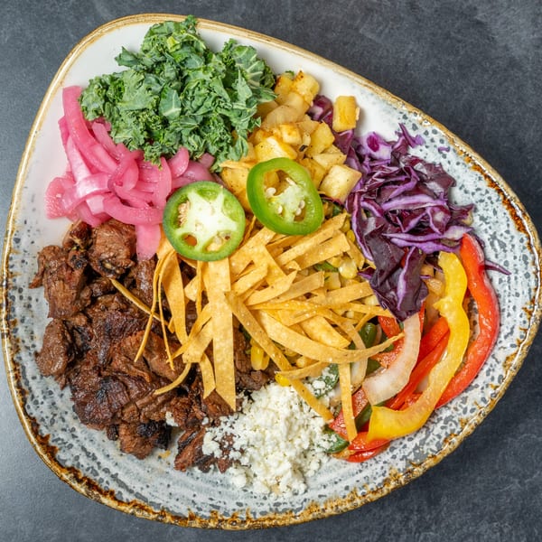 A colorful Mexican bowl with steak, kale, pickled onions, potatoes, jalapenos, and bell peppers.