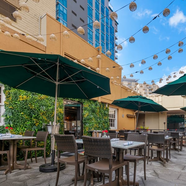 Guapo's Cocina & Bar's outdoor patio features tables with umbrellas, a green wall, and string lights.