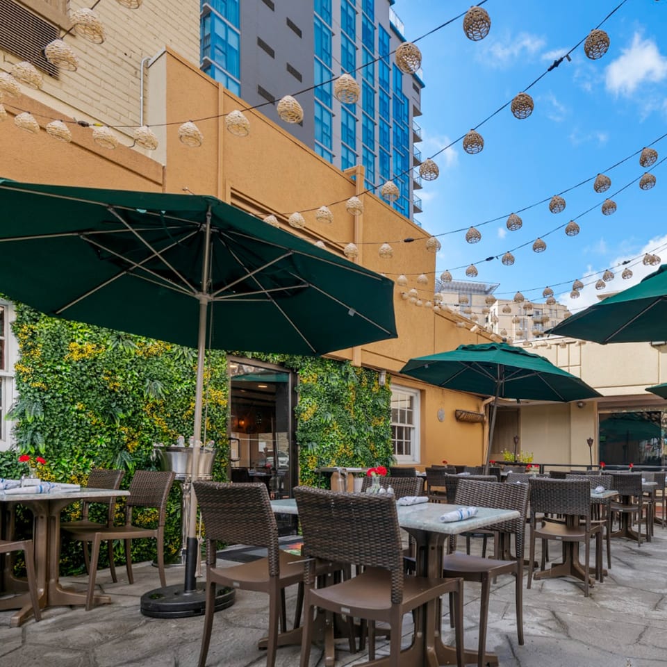 Guapo's Cocina & Bar's outdoor patio features tables with umbrellas, a green wall, and string lights.