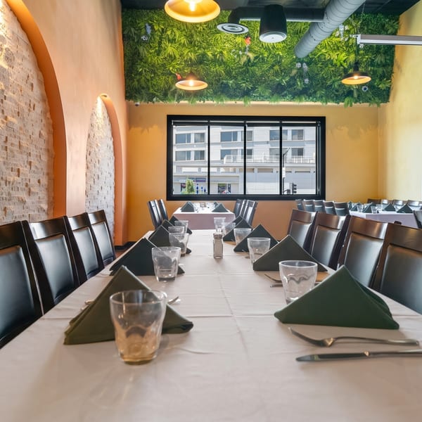 Restaurant dining room with long tables set with dark green napkins, black chairs, and a green ceiling.