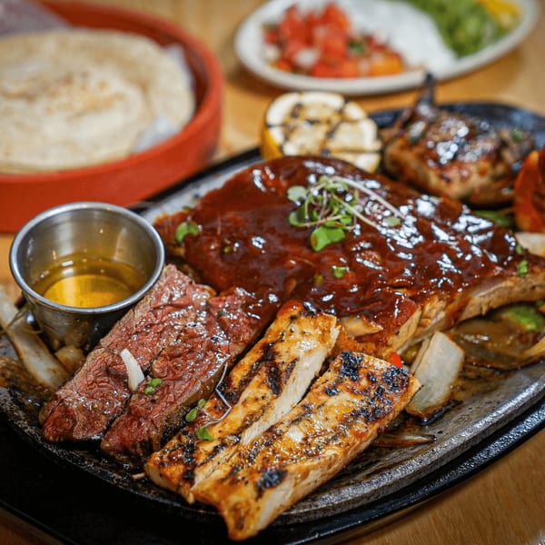 Sizzling platter of Guapo's ribs, steak, and chicken fajitas with tortillas and salsa.