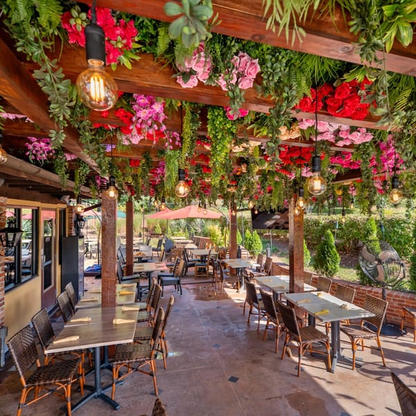 Guapo's Cocina & Bar's outdoor patio with tables, chairs, and a ceiling adorned with colorful flowers and greenery.