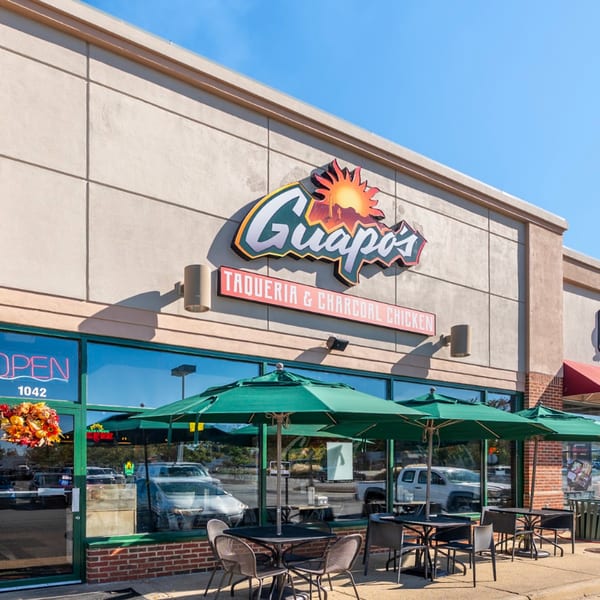 Exterior of Guapo's Taqueria & Charcoal Chicken, with outdoor seating under green umbrellas.