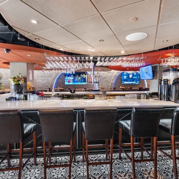 Interior view of Guapo's Cocina & Bar, showing a long bar with stools, hanging glasses, and TVs.